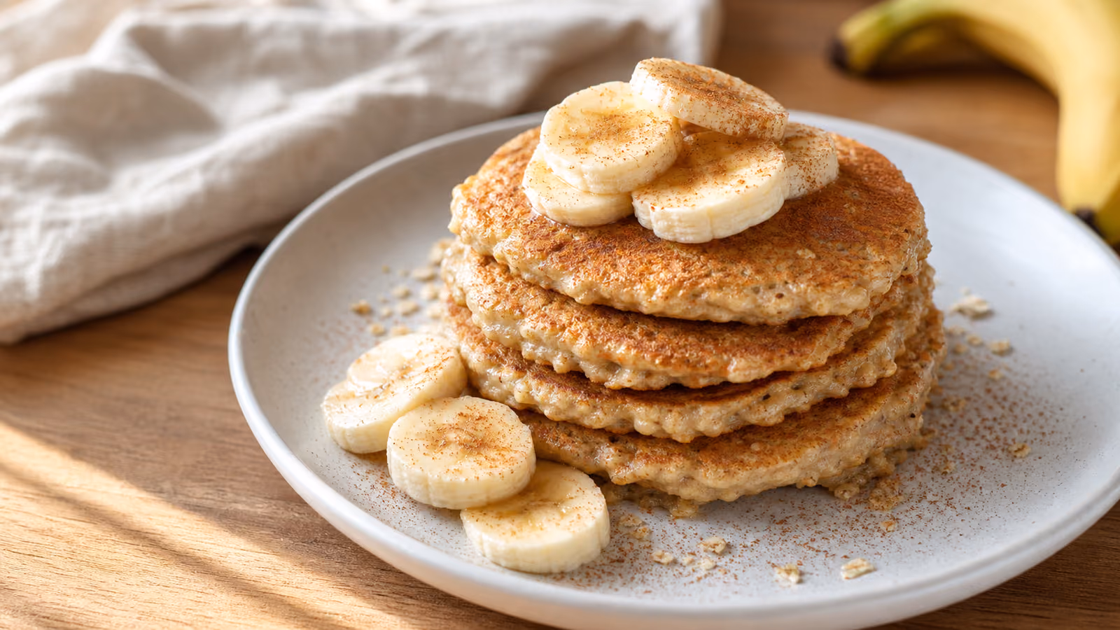 Pilha de panquecas de aveia e banana num prato branco, polvilhadas com canela